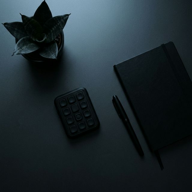 A matte black silent fidget pad on a dark desk beside a notebook and pen
